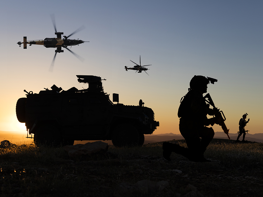 Battlefield with a soldier, armored vehicle and flying helicopters at sunset